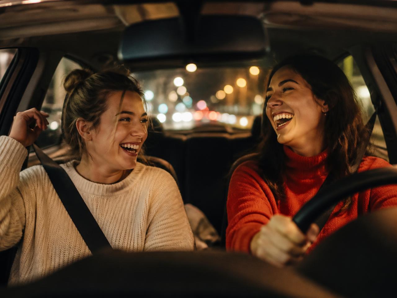 Duas amigas conversando e sorrindo dentro de um carro à noite